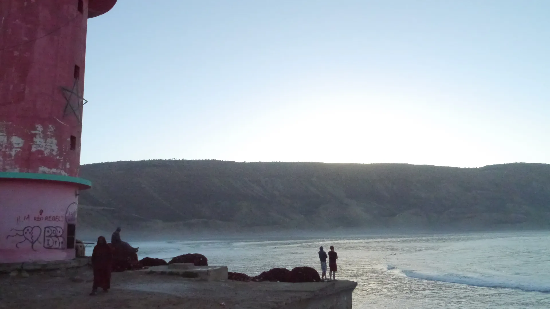 Imsouane Bay at sunrise — surfers lined up on the long right-hand wall of the Cathedral, one of the longest waves in North Africa