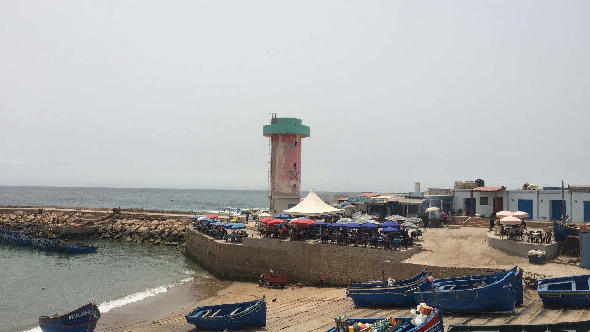 Blue fishing boats lined up in Imsouane's port — the lighthouse and the cafés in the background