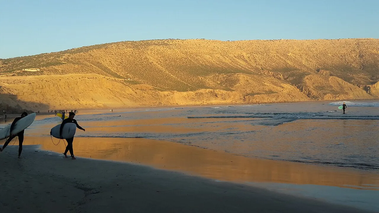 Sunset at Imsouane — surfers walking on the wet sand reflecting the warm light