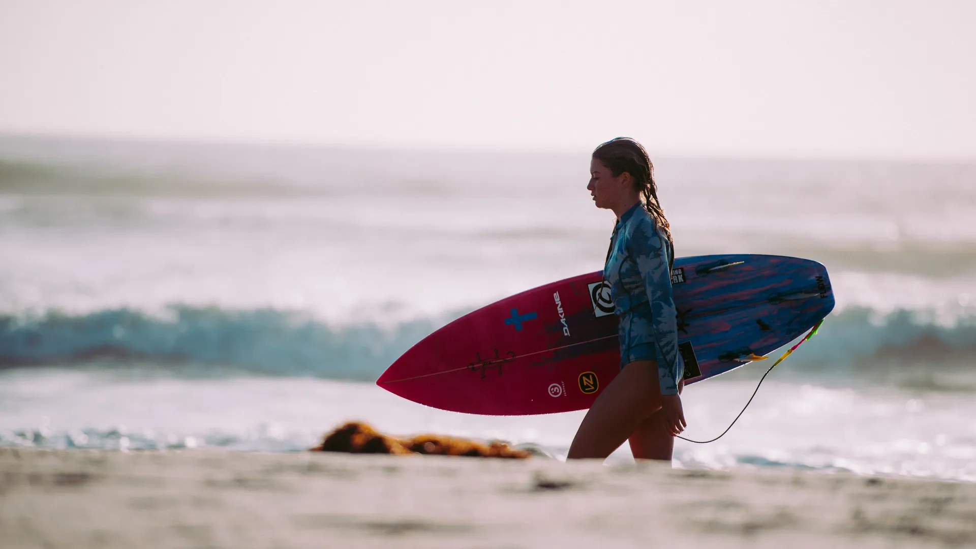 Surfer walking with a board along the sand — the image that sums up the Surf Village positioning of the Radisson Blu Taghazout Bay