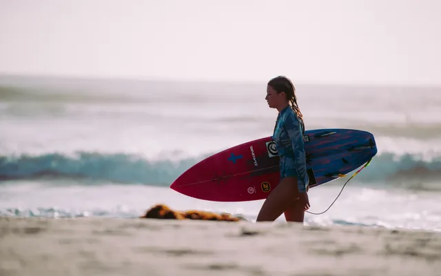 Surfer walking with a board along the sand — the image that sums up the Surf Village positioning of the Radisson Blu Taghazout Bay