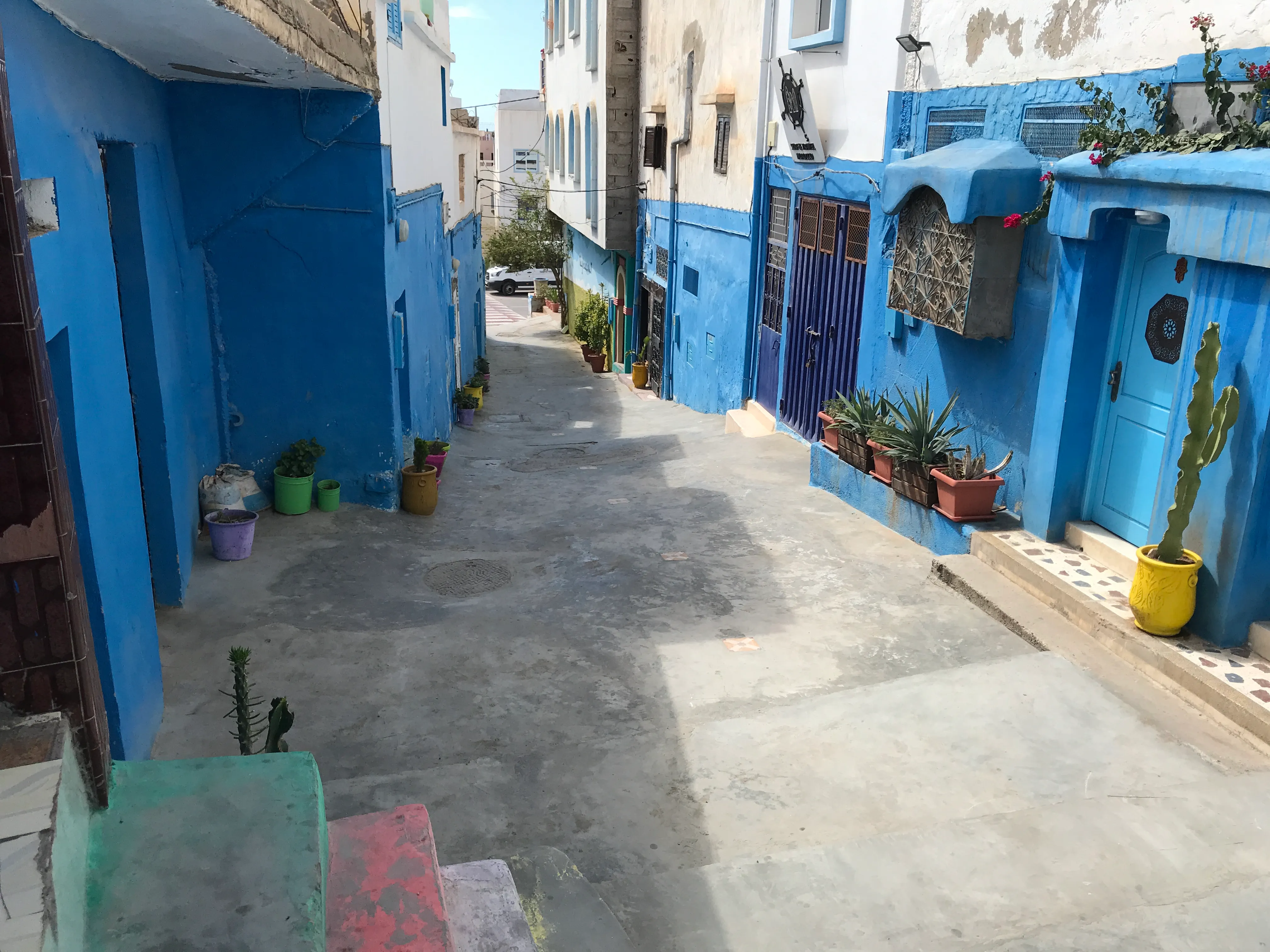 The narrow whitewashed streets of Taghazout village — surfers walking with boards, blue doors, a cat sleeping in a doorway