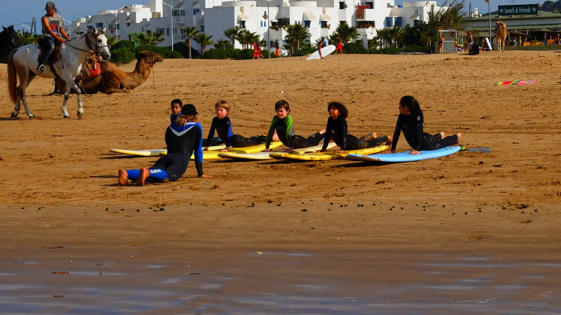 Boutiques et écoles de surf alignées le long d'une rue de village marocain — l'offre locale qui s'est développée autour de Tamraght depuis les années 2010